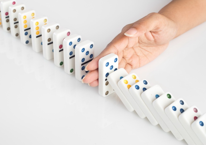 Human hand stopping a line of dominoes from falling. concept image for recovery plan and solution for cascading failures and problems. Dominoes are placed on a white table. High key image shot in studio.