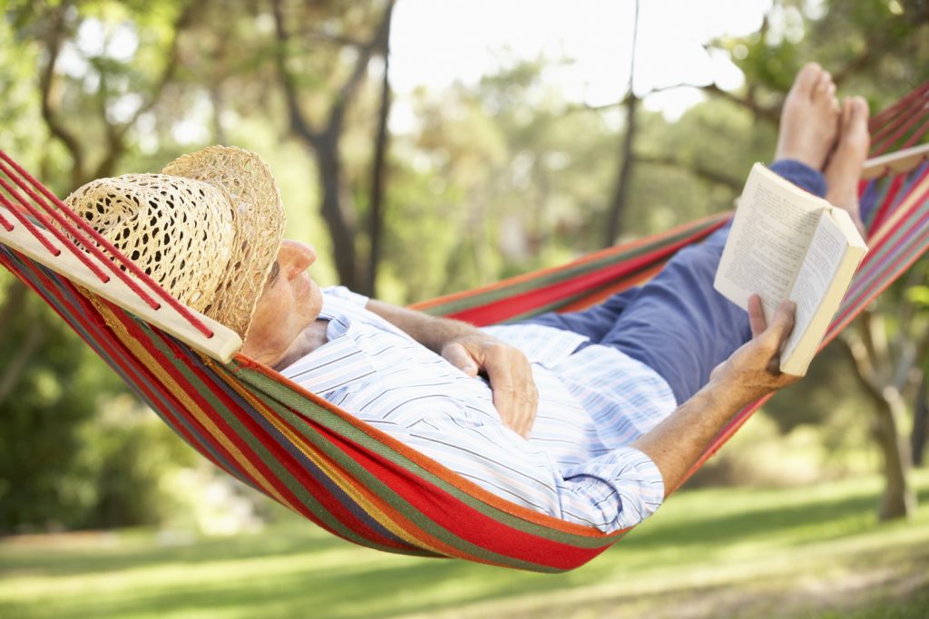 Senior Man Relaxing In Hammock With Book