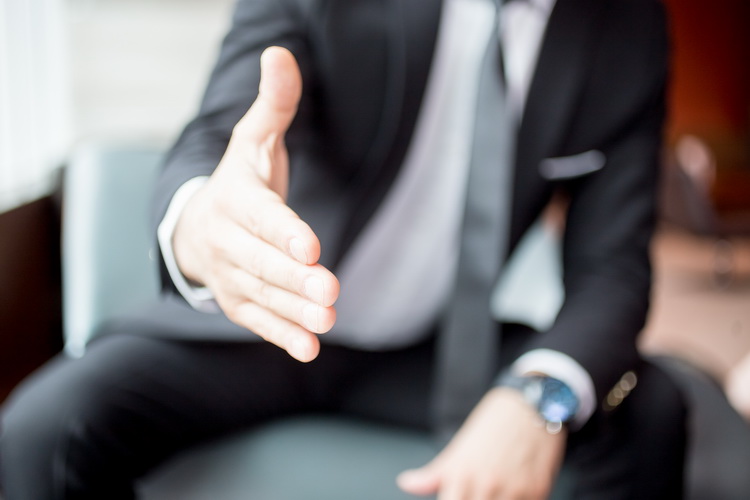 Cropped view of business man sitting and extending arm for handshake with focus on hand